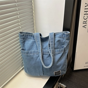 Minimalist blue denim tote bag with dual front pockets and woven label on a windowsill