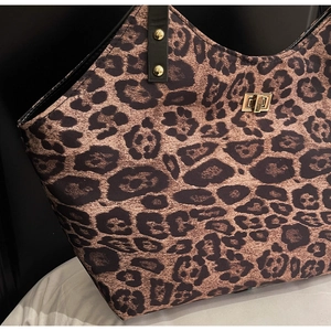 Close-up of leopard print tote bag with black leather handle and golden metal lock detail