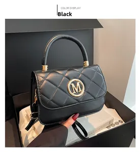 Detail of black quilted shoulder bag featuring gold M logo and rigid top handle