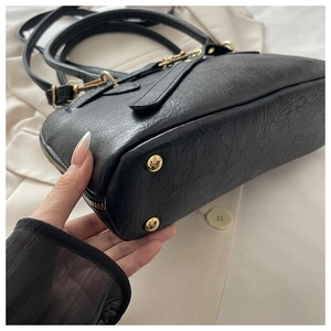 Detail of black vintage leather bag showing golden metal studs and reinforced bottom structure
