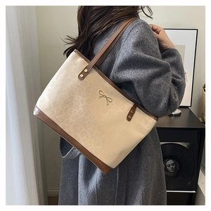 Detailed view of leopard print tote bag with gold bow accent worn with wool coat