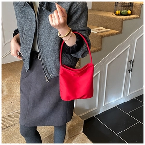 Détail du sac seau rouge en nylon avec logo gaufré tenu par un mannequin en escalier