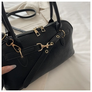 Close-up of black leather handbag featuring premium gold hardware and dual zipper detail