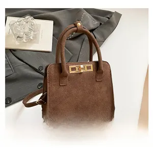 Detail of dark brown suede tote bag featuring a golden metal twist lock and dual handles