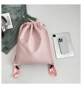 Flat lay of pink nylon drawstring backpack with lifestyle accessories on white background
