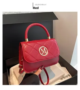 Detail of red quilted handbag featuring a golden M logo and adjustable shoulder strap