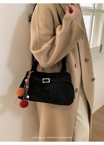 Detail of black suede shoulder bag with silver buckle and colorful pom-pom pendant