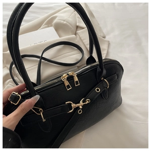 Detailed view of black leather handbag featuring premium gold zippers and metal hardware