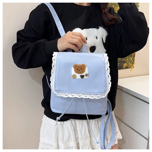 Detail view of light blue backpack with lace trim and plush bear patch decoration