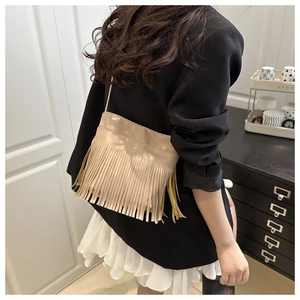 Détail du sac bandoulière beige clair à franges porté avec une tenue urbaine chic