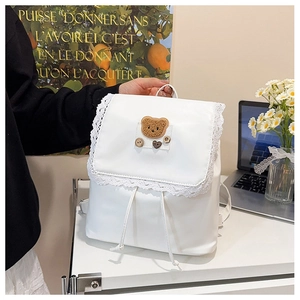 Detail of white lace-trimmed backpack featuring a cute teddy bear plush patch and vintage buttons