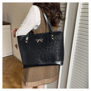 Detail of black leopard print tote bag with golden bow clasp on a lifestyle model view
