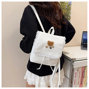Detailed shot of white canvas backpack with lace edges and a plush bear patch