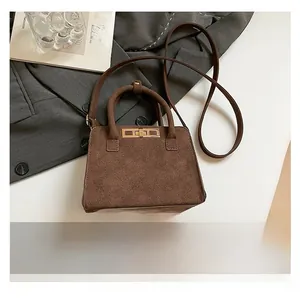 Detail of dark brown suede handbag with gold lock and mobile phone for size reference