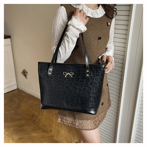 Lifestyle shot of black leopard print tote bag with gold bow on brown dress model