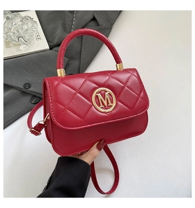 Close-up of red quilted handbag with golden M logo and glossy leather texture