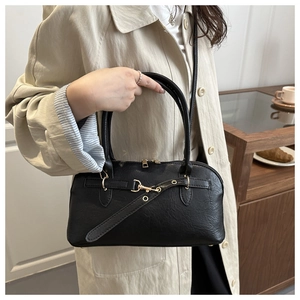 Detail of elegant black PU leather handbag with gold buckle held by a model in a beige coat