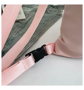Detail of pink nylon backpack featuring woven shoulder strap and black plastic buckle