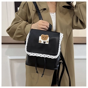 Detail of black faux leather backpack with white lace trim and cute bear patch