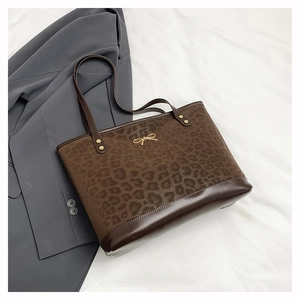 Detail of leopard print tote bag featuring golden bow metal piece and dark brown leather trim