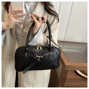 Detail of minimalist black shell bag with textured leather and gold-tone metal hardware