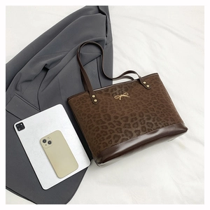 Close-up of leopard print tote bag with gold bow accent and brown leather straps