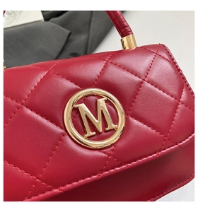 Detail of burgundy quilted leather bag with a circular gold M logo emblem and stitching