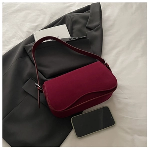 Detail of burgundy suede shoulder bag with curved flap and silver hardware on a grey blazer
