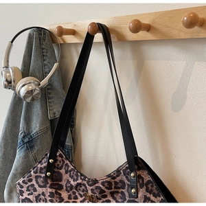 Close-up of leopard print tote bag featuring black leather straps and metal rivets