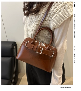 Detail of a deep brown patent leather handbag with silver buckle worn by a model