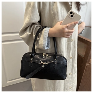 Close-up of a black faux leather handbag with vintage belt decor and gold buckles on a model