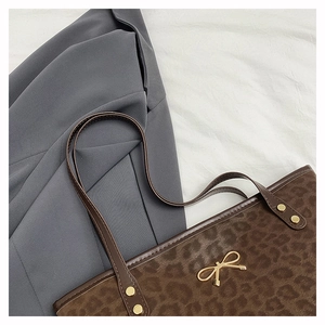 Detail of leopard print tote bag with gold bow ornament and rivet handles on blazer