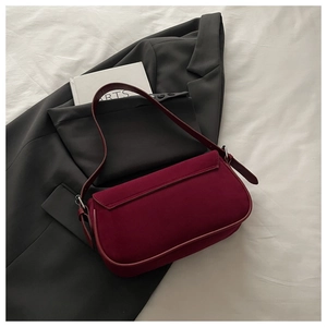 Detail shot of a minimalist burgundy suede baguette bag on a grey blazer and white linen