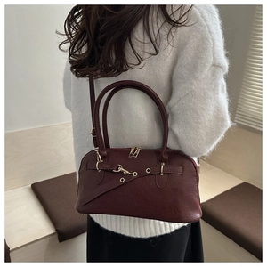 Detail of burgundy leather handbag with metal buckle strap and golden hardware