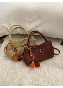 Detail of minimalist suede tote bags with decorative charms and adjustable shoulder straps