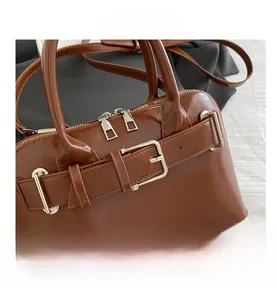 Detail view of brown glossy PU leather handbag with silver buckles and dual zip closings