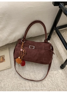 Macro detail of brown suede tote bag with decorative tassel and metal buckle on fur rug