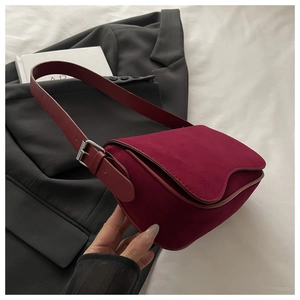 Detail of burgundy frosted shoulder bag with wavy flap design on white bedding