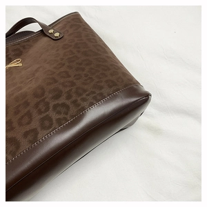 Close-up of leopard print tote bag with brown leather stitching and gold metal accents