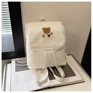 Detail of white lace backpack featuring a cute brown bear patch and metal buckles
