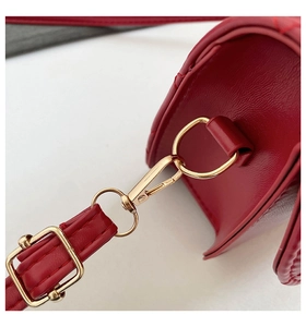 Detail of red leather bag showing golden metal lobster clasp and adjustable shoulder strap