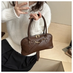 Close-up of deep brown leather shoulder bag featuring metal eyelet straps and gold zippers