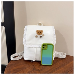 Close-up of white mini backpack featuring lace trim and a brown plush bear patch