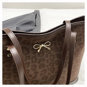 Close-up of leopard print suede tote bag with golden bow hardware and leather trim