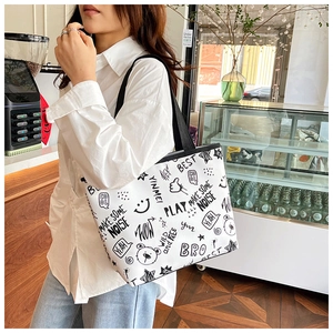 Detail of white canvas tote bag featuring black graffiti prints and sturdy black shoulder straps