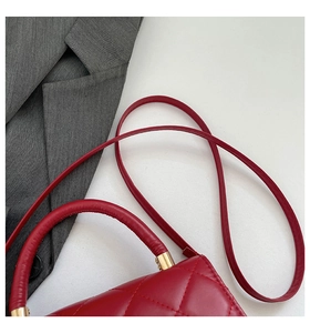 Close-up of red quilted handbag with golden metal hardware and round handle detail