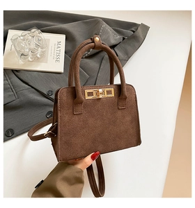 Detail view of brown matte handbag featuring golden twist lock and elegant top handle