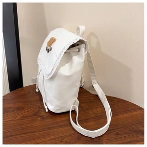 Detail of white PU leather backpack featuring lace edges and a brown bear patch detail