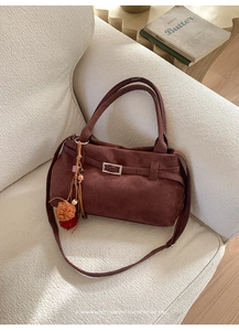 Detail of a brown vintage suede tote bag with decorative straps on a beige fabric sofa