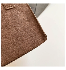 Detailed close-up of brown frosted suede leather texture and neat stitching on shoulder bag